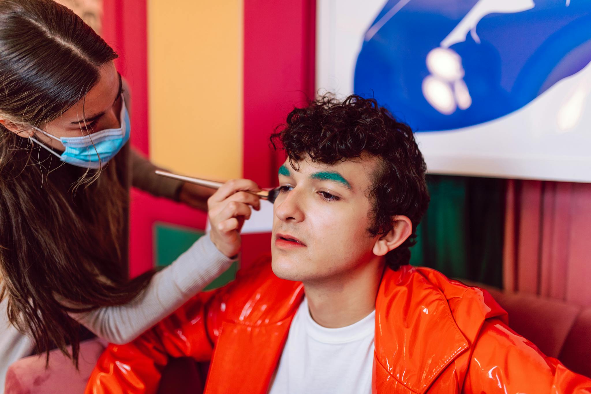 A makeup artist carefully applies vivid eyeshadow to a person indoors, showcasing vibrant colors and artistry.